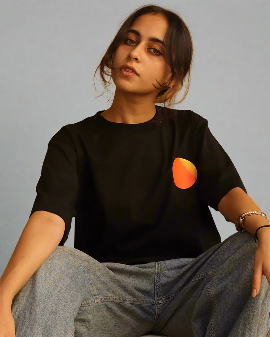 Woman sitting wearing a black t-shirt, With a bright orange sun in the front at the pocket side