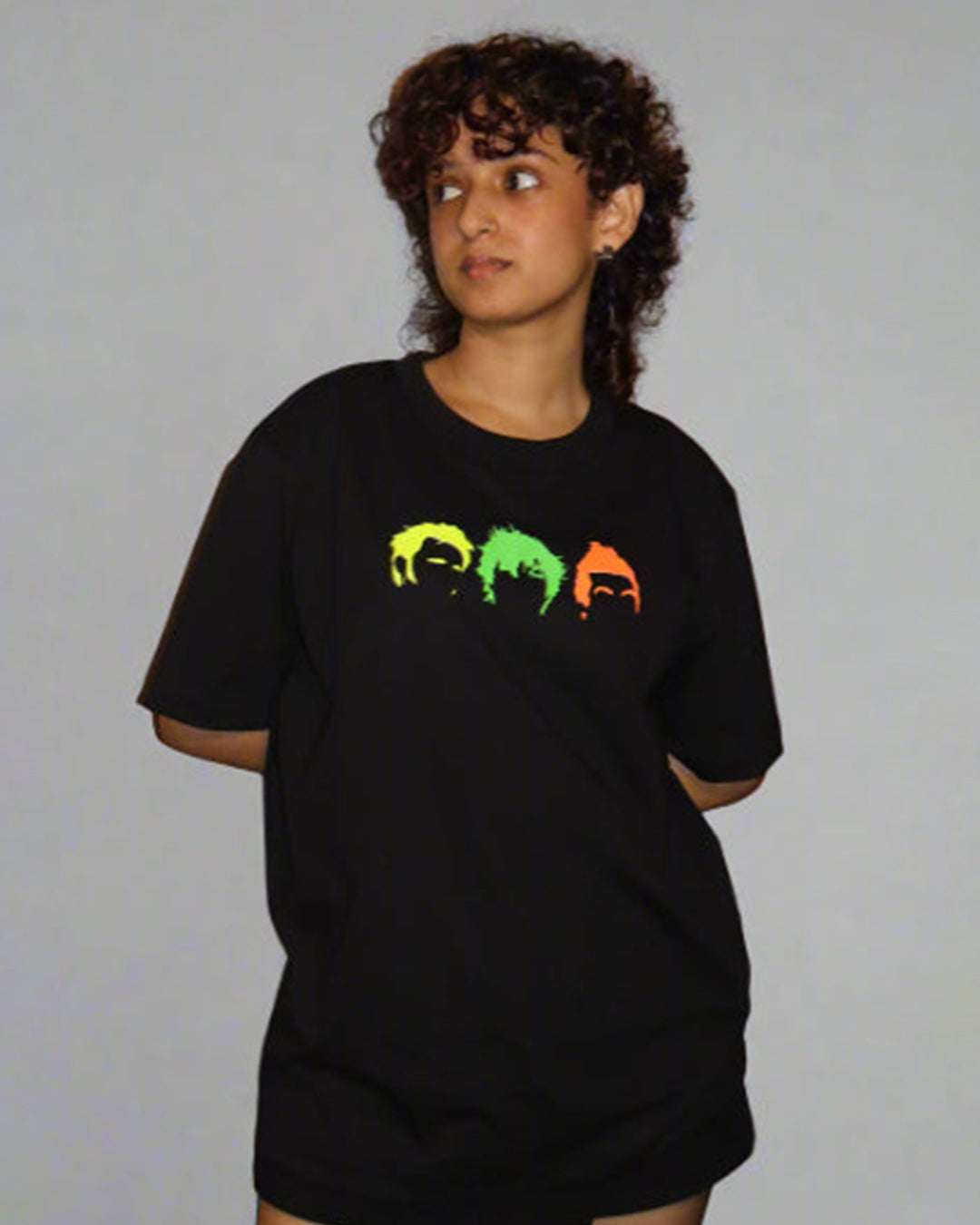 woman wearing black tshirt with three head/hair outlines in the front , in the colour yellow green and orange