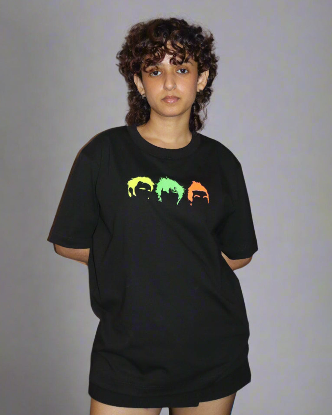 woman wearing black tshirt with three head/hair outlines in the front , in the colour yellow green and orange