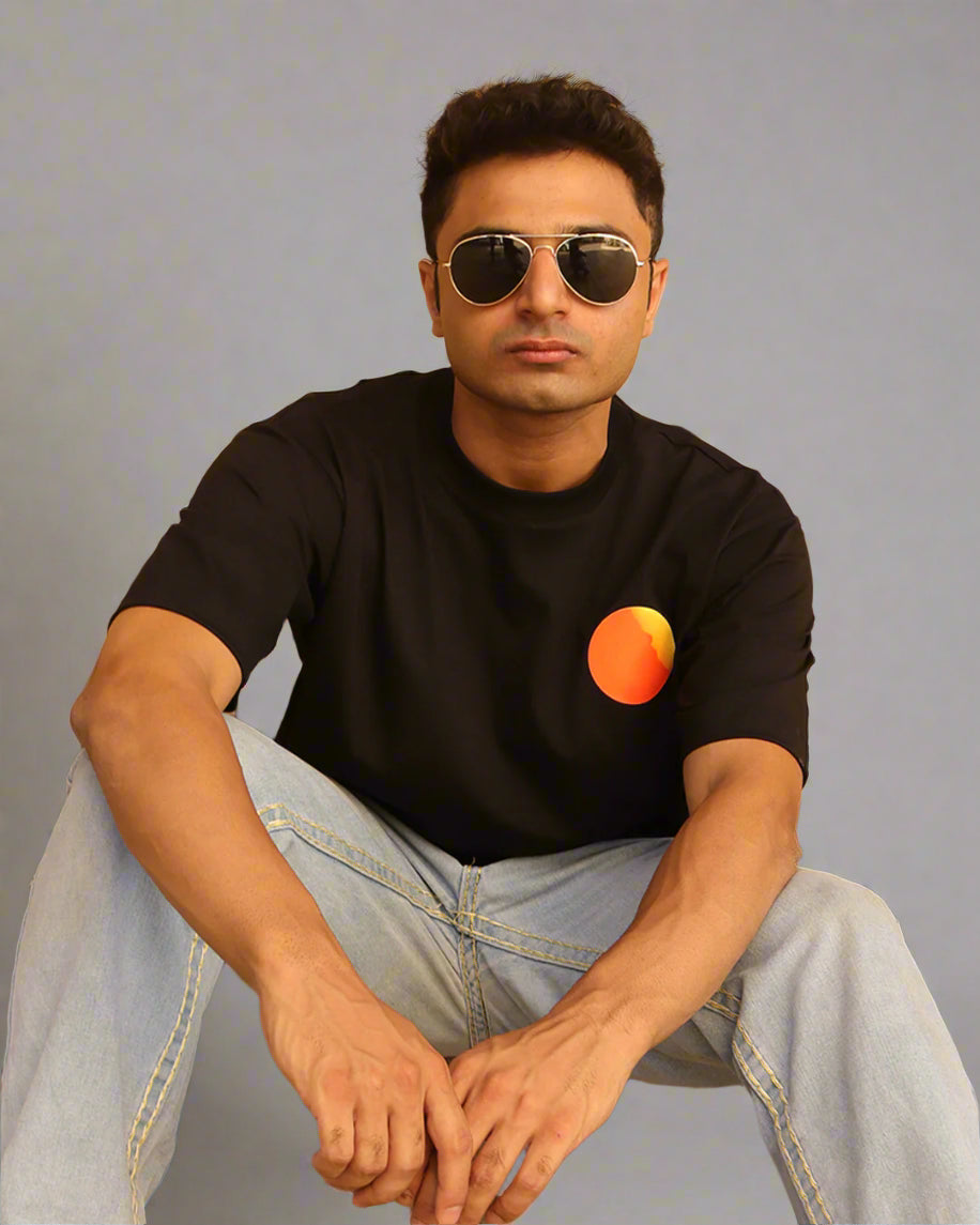 Man sitting wearing a black t-shirt, With a bright orange sun in the front at the pocket side