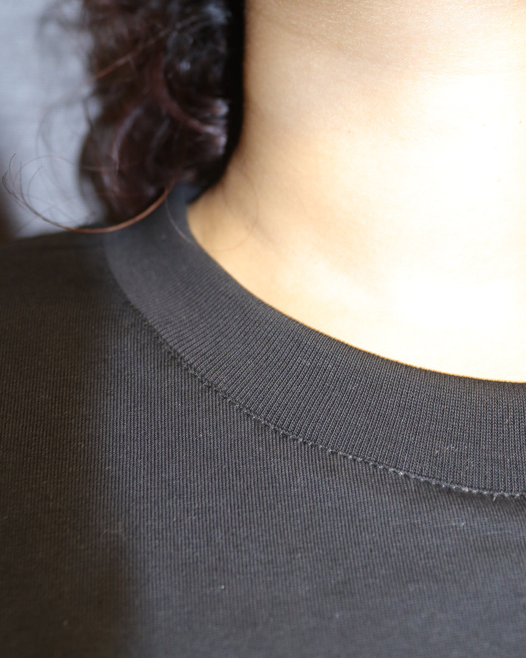 woman showcasing her tshirts neck and the stitches in t , wearing a black tshirt