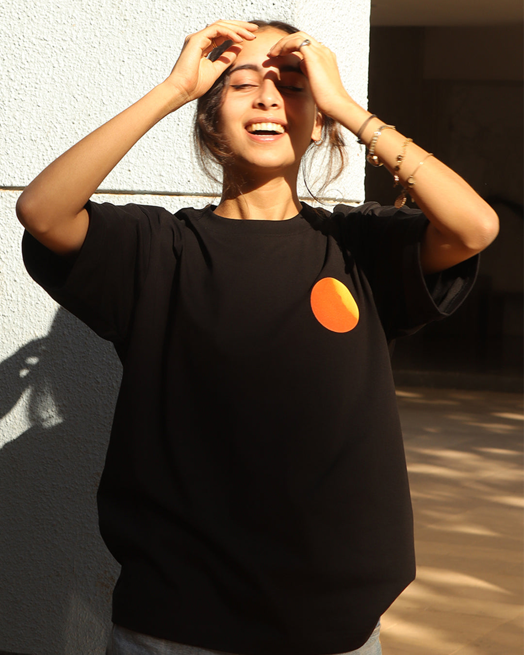 Woman sitting wearing a black t-shirt, With a bright orange sun in the front at the pocket side
