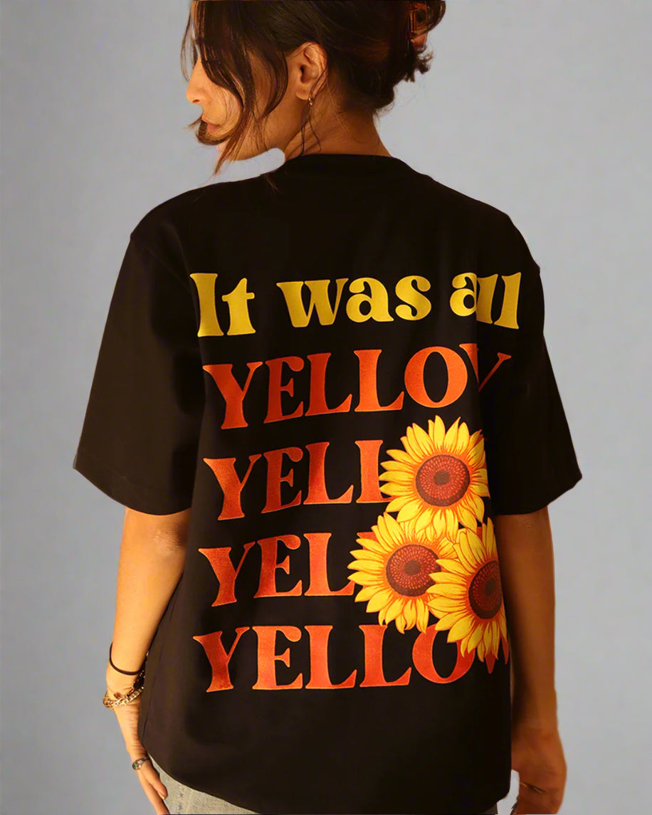 Woman standing wearing a black t-shirt, With a bright orange sun in the front at the pocket side and it was all yellow written in the back