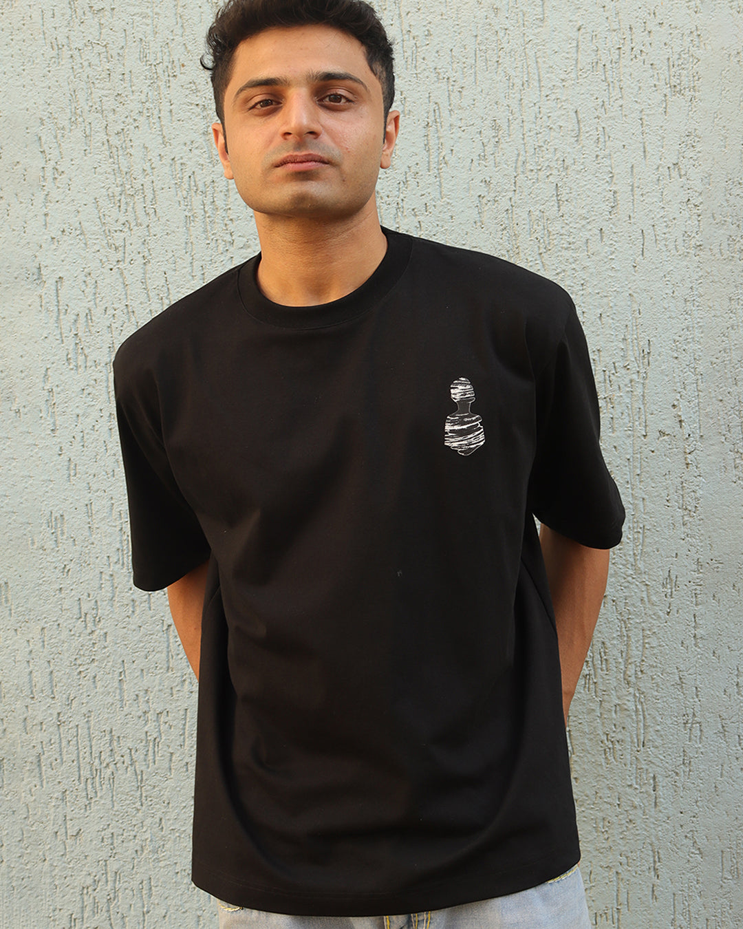 Man standing wearing a black t-shirt, With a art in the front at the pocket side
