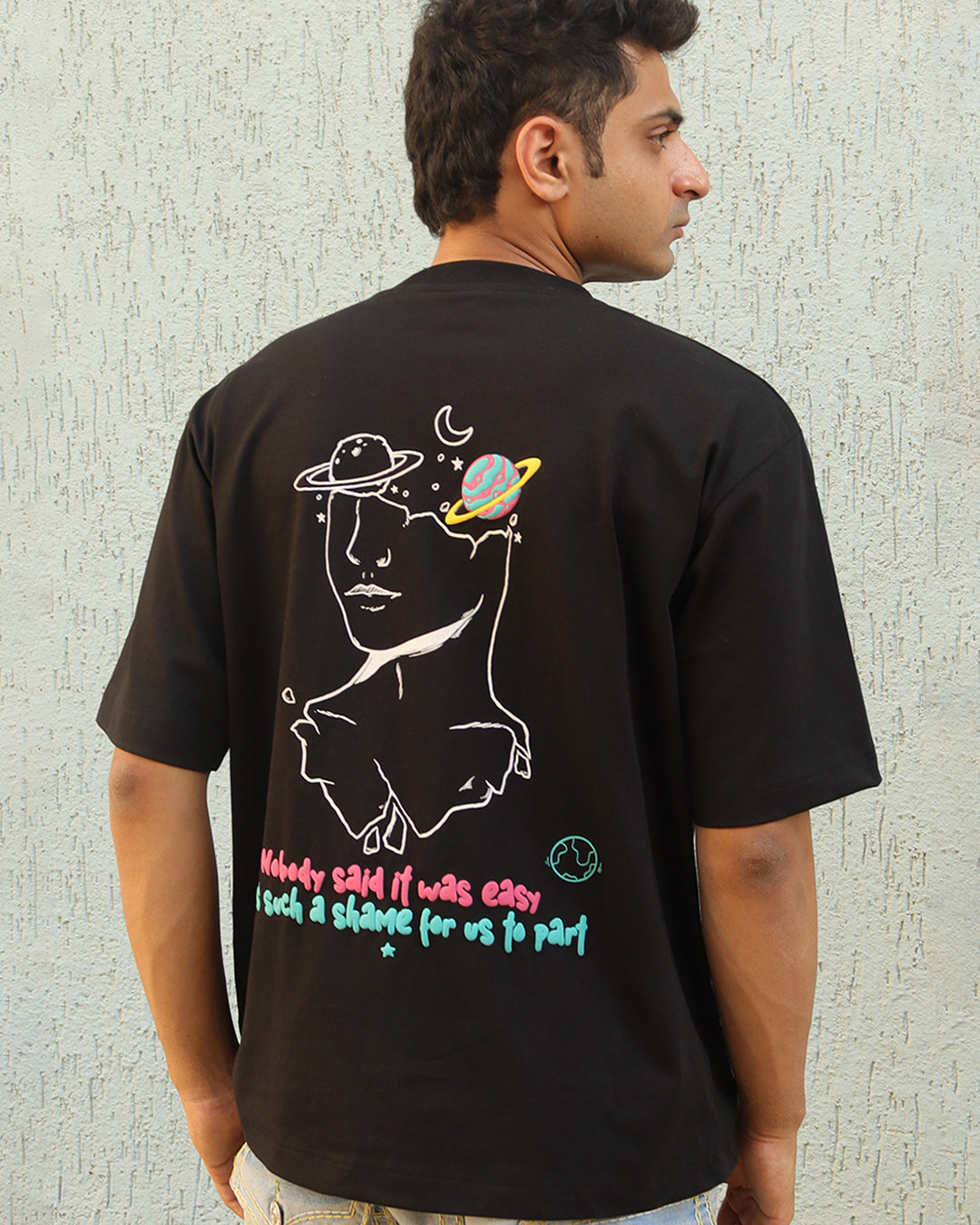 Man standing wearing a black t-shirt, With a art in the front at the pocket side and art and "nobody said it was easy , its such a shame for us to part" written on the back