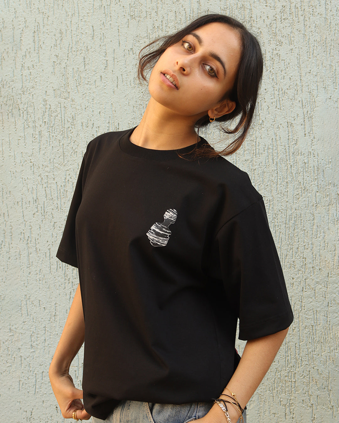 Woman standing wearing a black t-shirt, With a art in the front at the pocket side and art