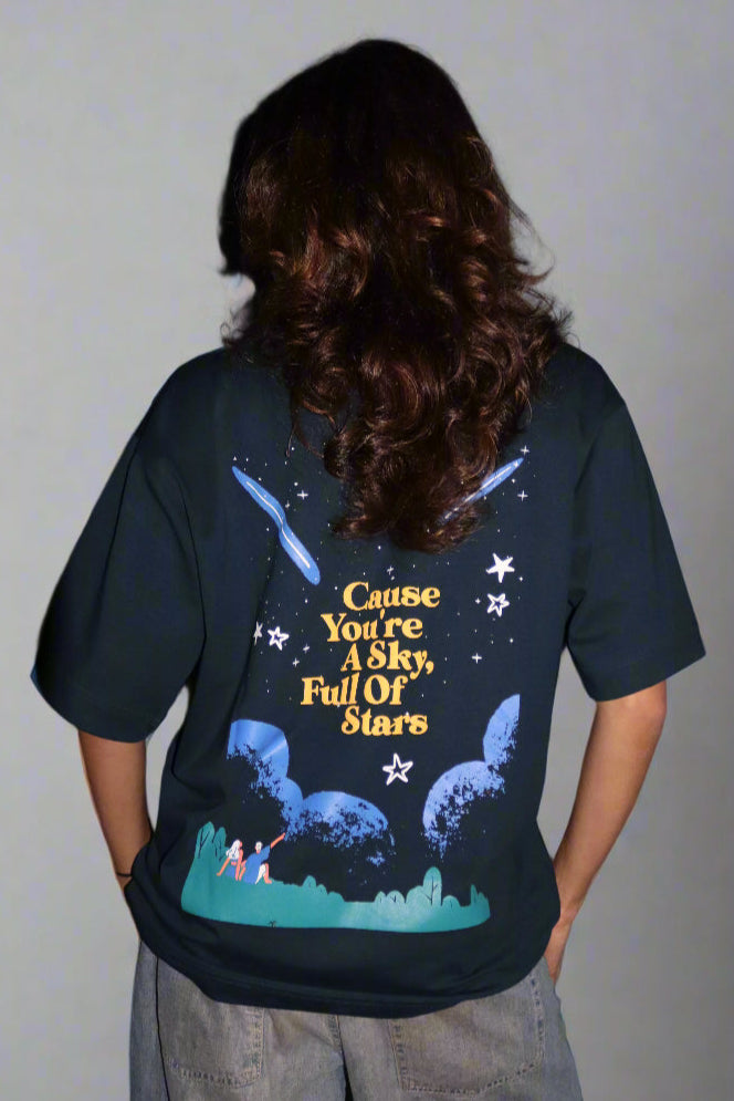 Woman standing wearing a dark blue t-shirt, With Cohrt written in the front and "Cause you're a sky full of stars" written on the back.
