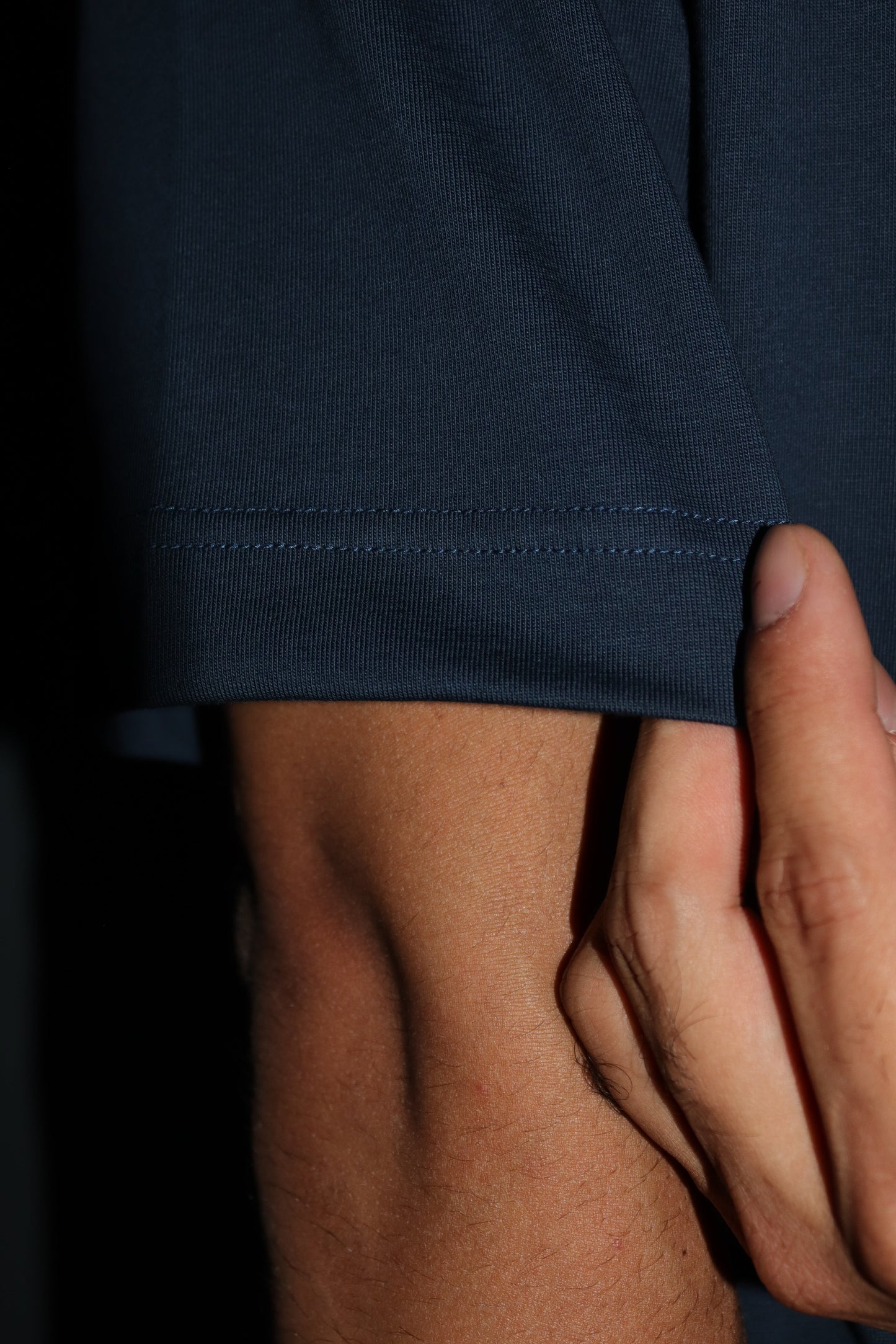 Man standing wearing a dark blue t-shirt and showing of his sleeves and stitches