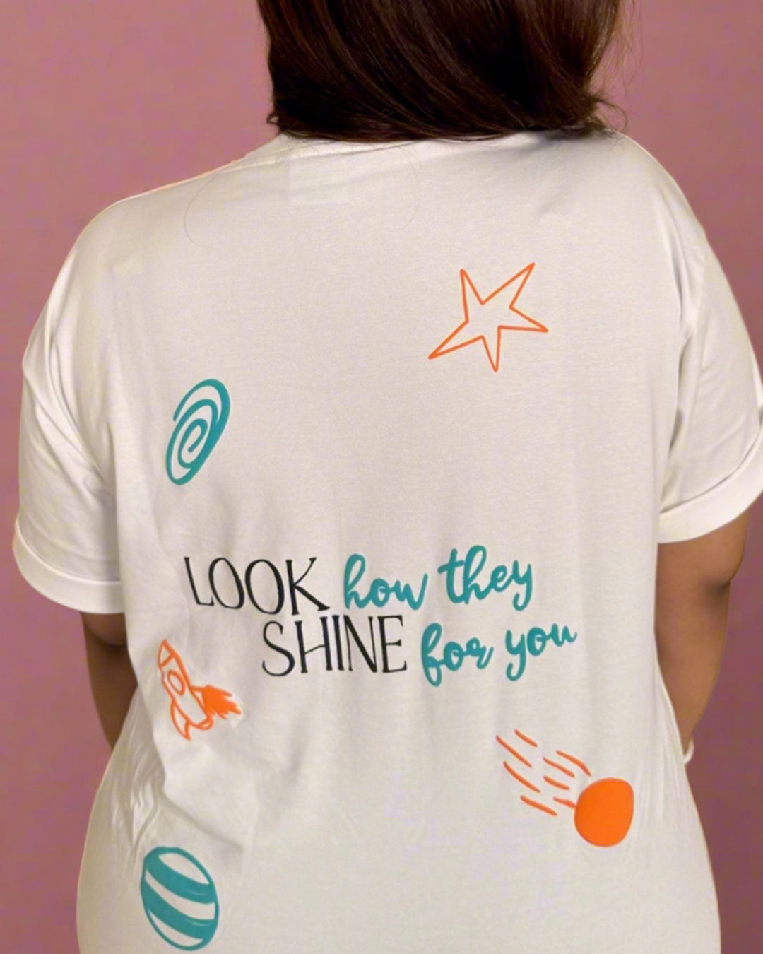 Woman standing wearing a White t-shirt, with Look how they shine for you written in the back