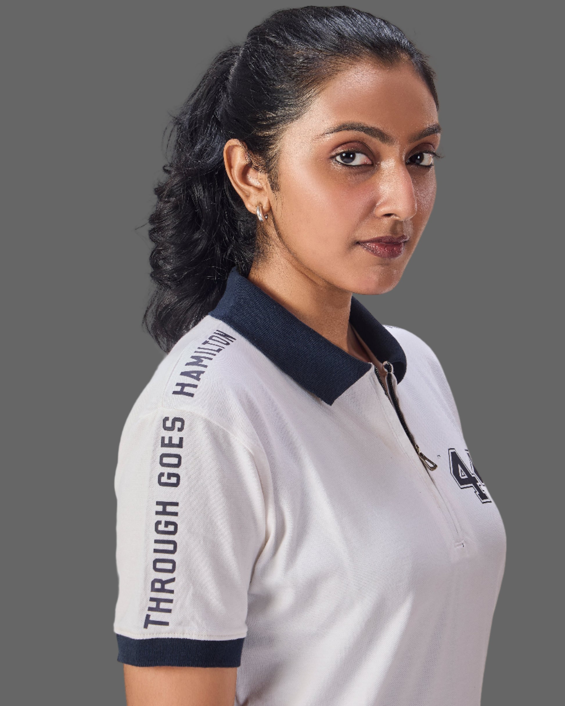 Woman wearing a white polo shirt with through goes hamilton written on the sleeves and 44 in the front  on a plain background