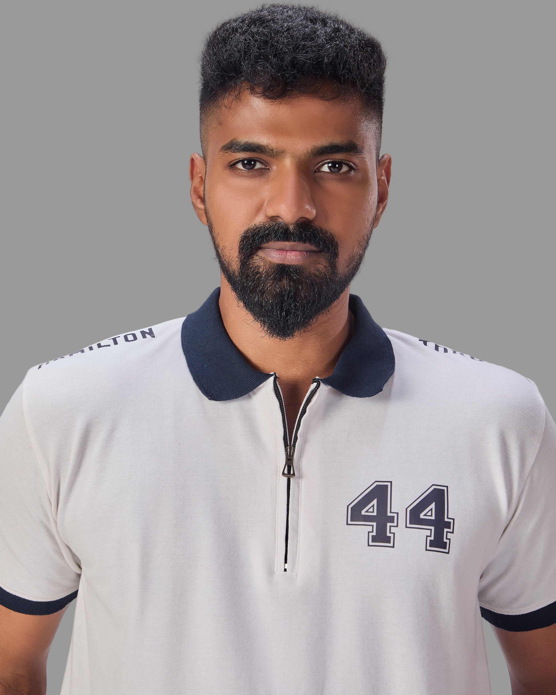 Man wearing a white polo shirt with a navy collar and number 44 with through goes hamilton written on the sleeves and 44 in the front  on a plain background