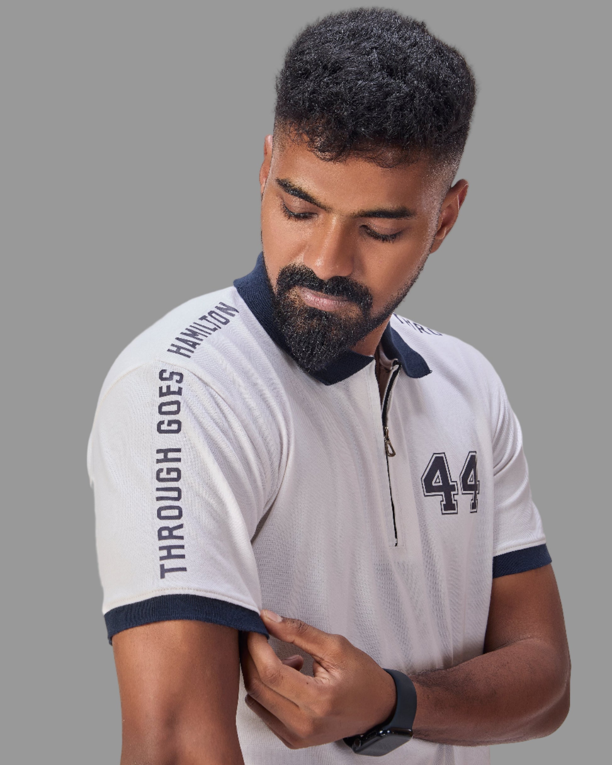 Man wearing a white polo shirt with with through goes hamilton written on the sleeves and 44 in the front  on a plain background