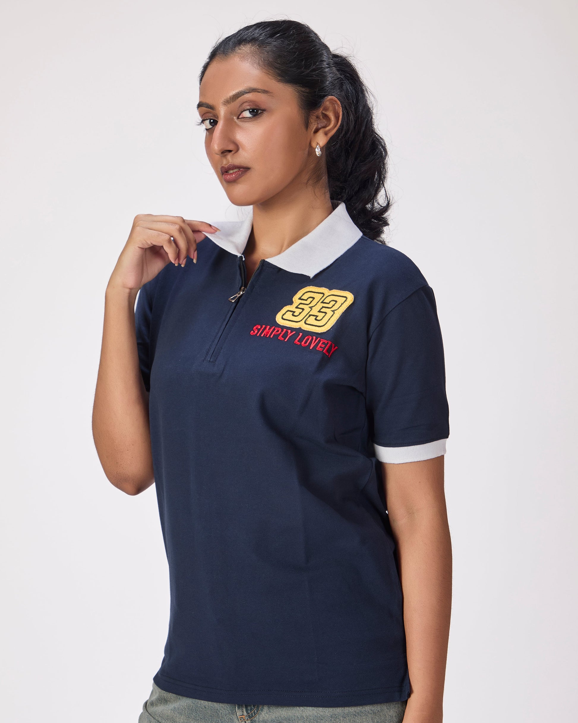 Woman wearing a navy blue polo shirt with 33 and simply lovely embroidered on the front and a bull on the side on a white background