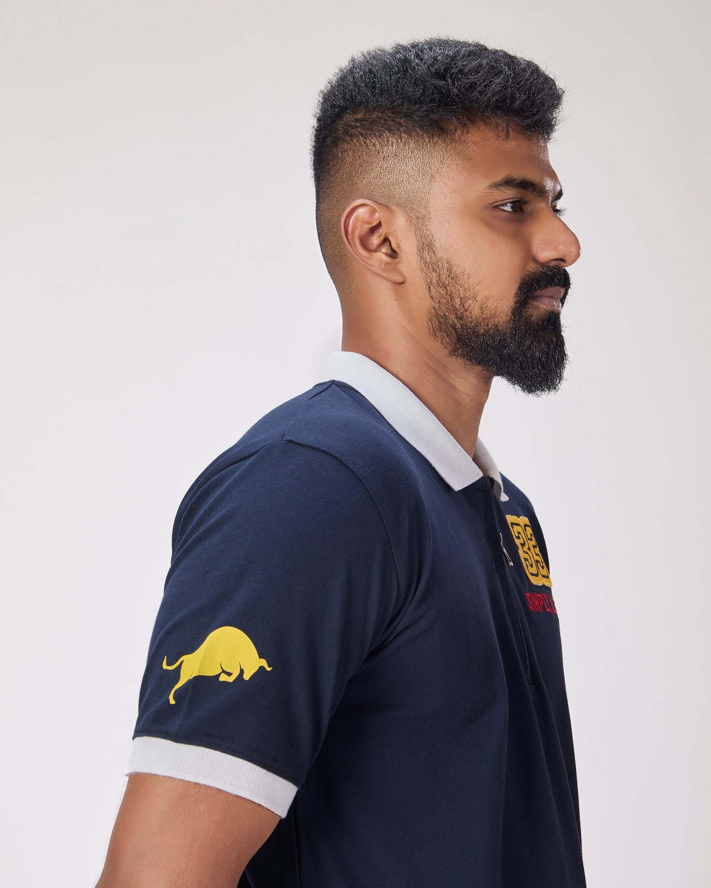 Man wearing a navy blue polo shirt with bull on sleeves and chest against a white background