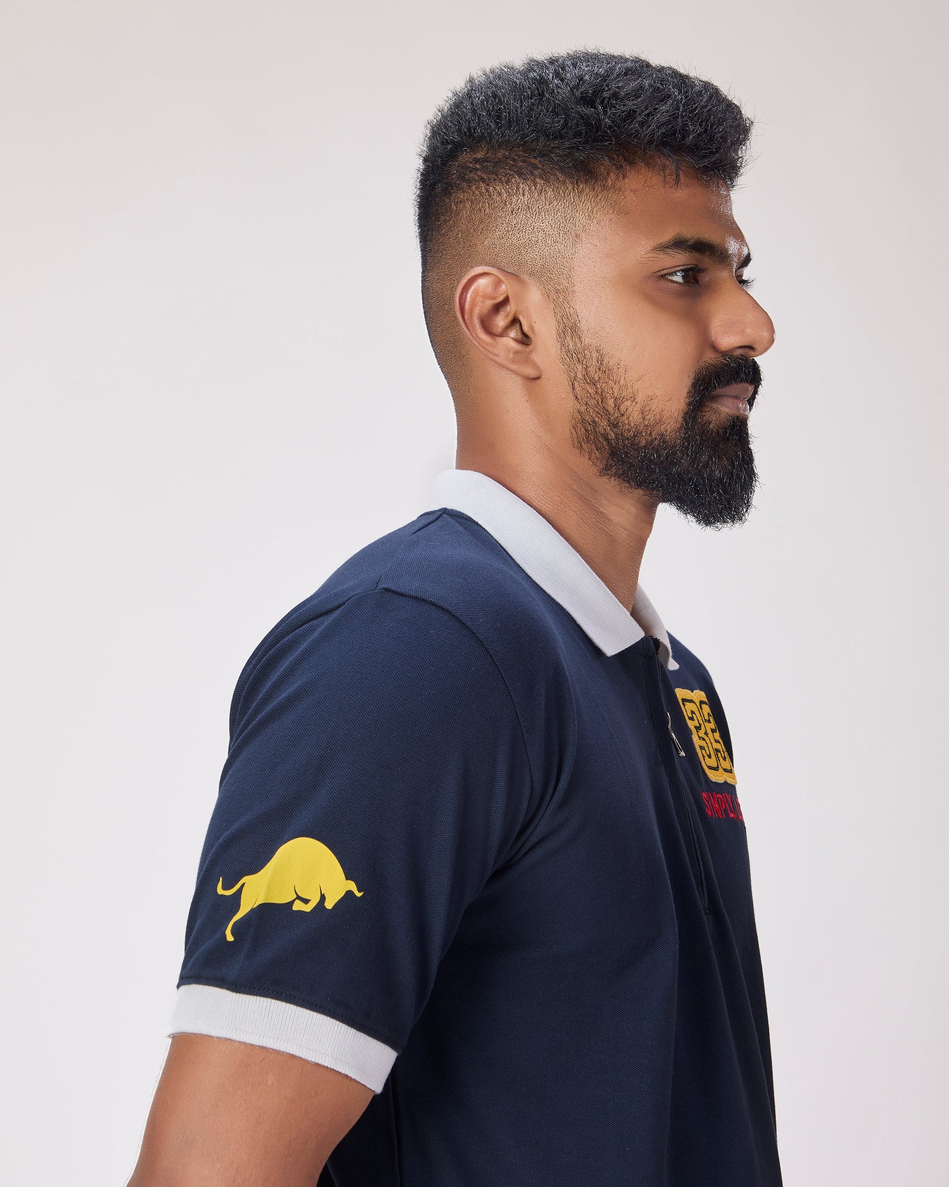 Man wearing a navy blue polo shirt with bull on sleeves and chest against a white background