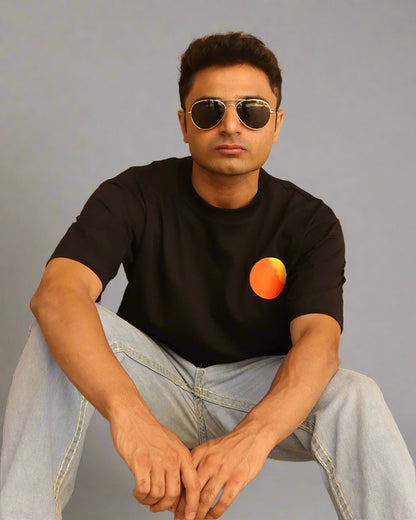 Man sitting wearing a black t-shirt, With a bright orange sun in the front at the pocket side