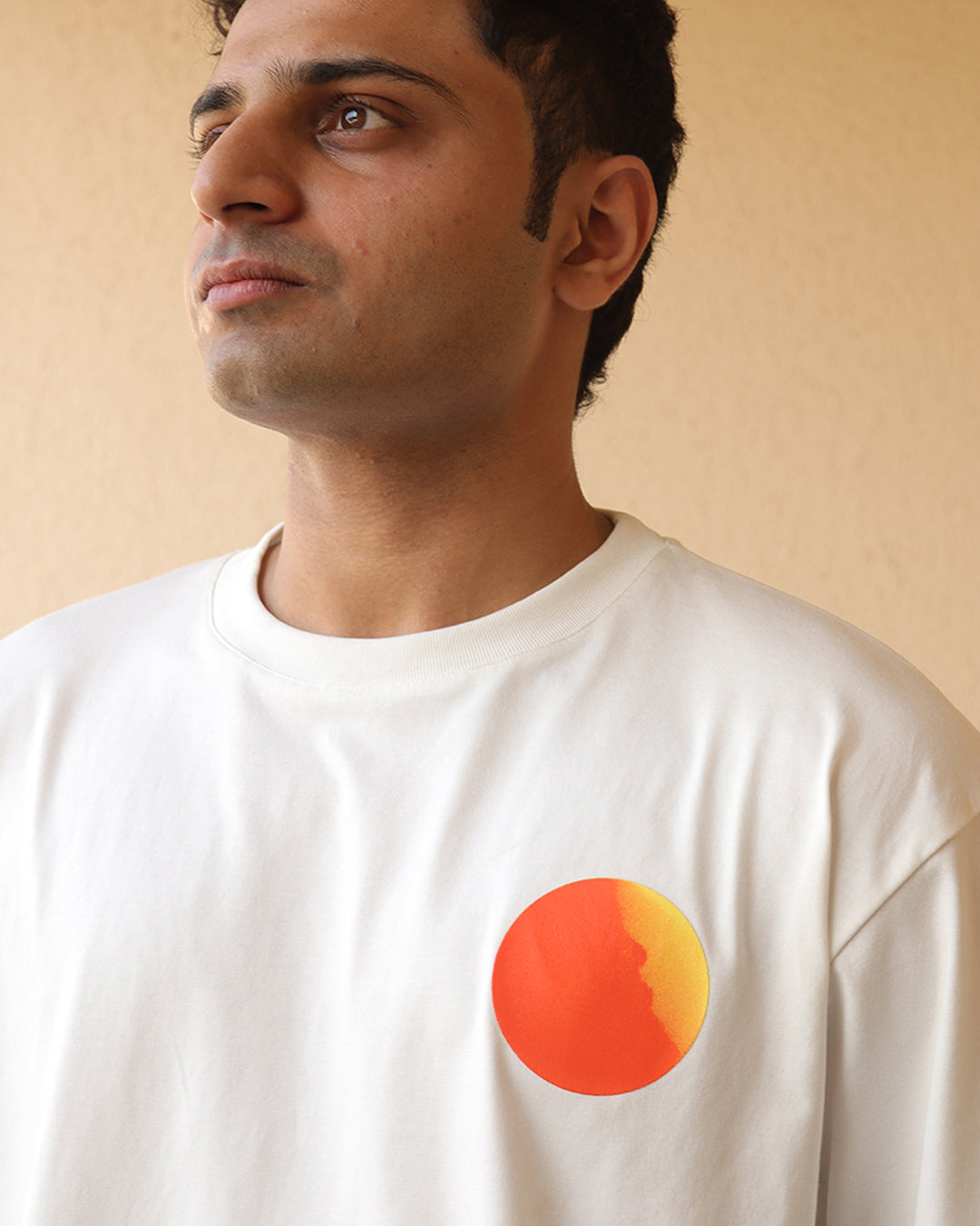 Man standing wearing a White t-shirt, With a bright orange sun in the front at the pocket side 