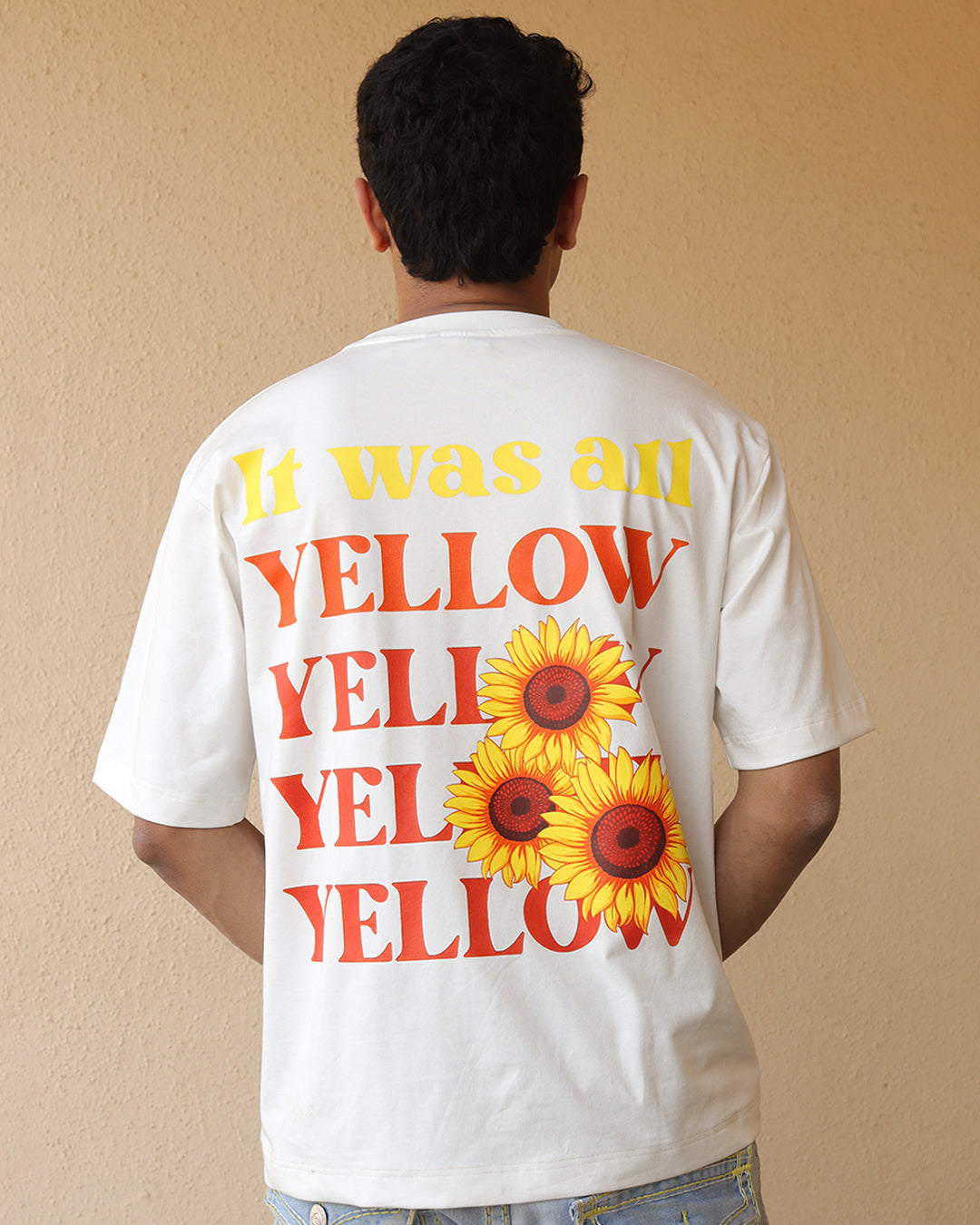 Woman standing wearing a  white t-shirt, With a bright orange sun in the front at the pocket side and it was all yellow written in the back