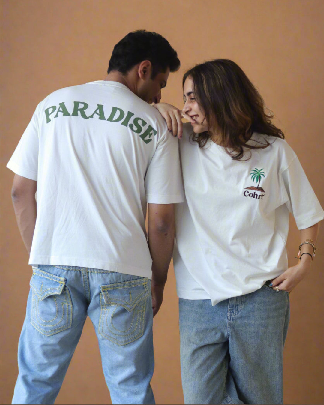 Woman and man standing Wearing white t-shirt and Palm tree on the pocket side and pardise written on the back