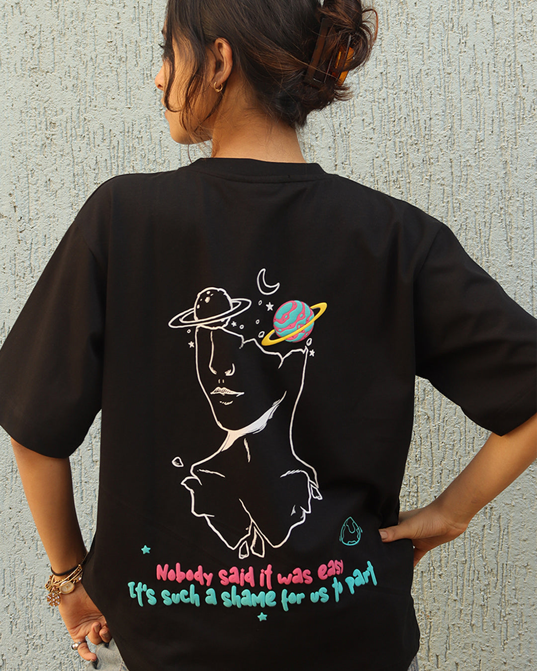 Man standing wearing a black t-shirt, With a art in the front at the pocket side and art and "nobody said it was easy , its such a shame for us to part" written on the back