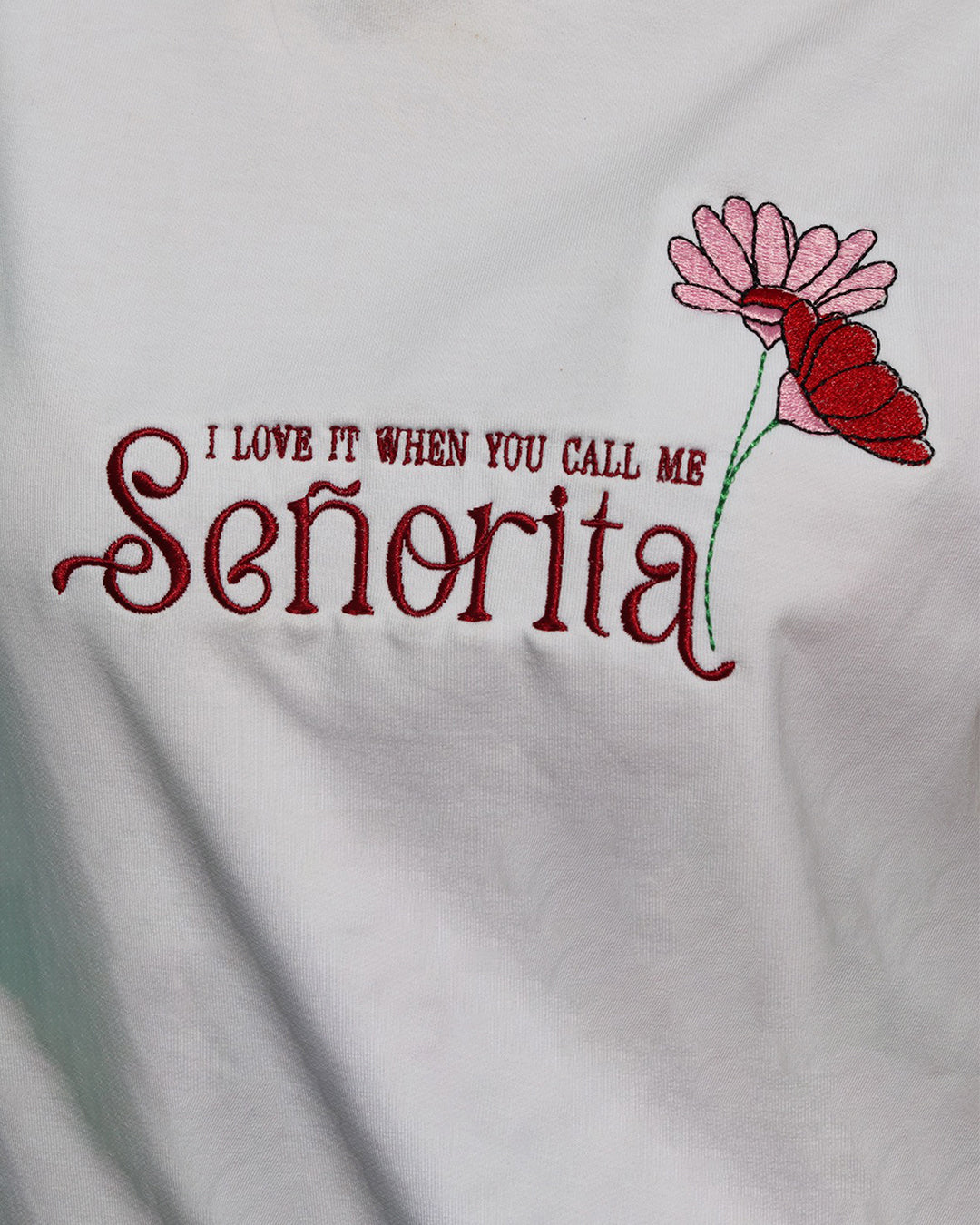woman wearing white tank top with i love it when you call me senorita embroided on the front