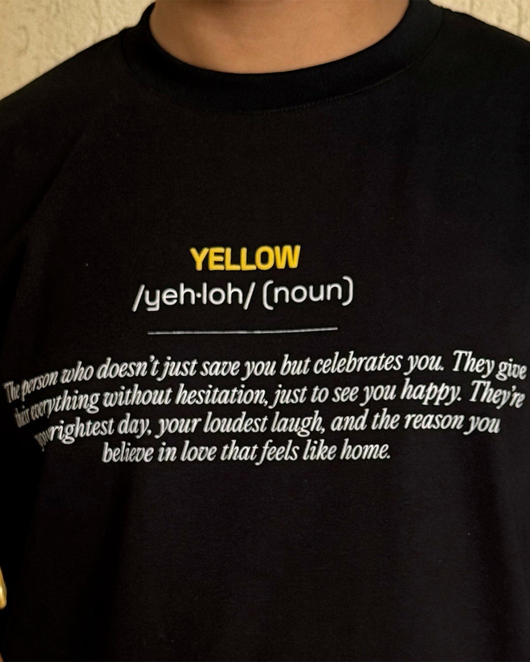 Man , standing wearing a Black t-shirt, with Yellow and its meaning written in the front