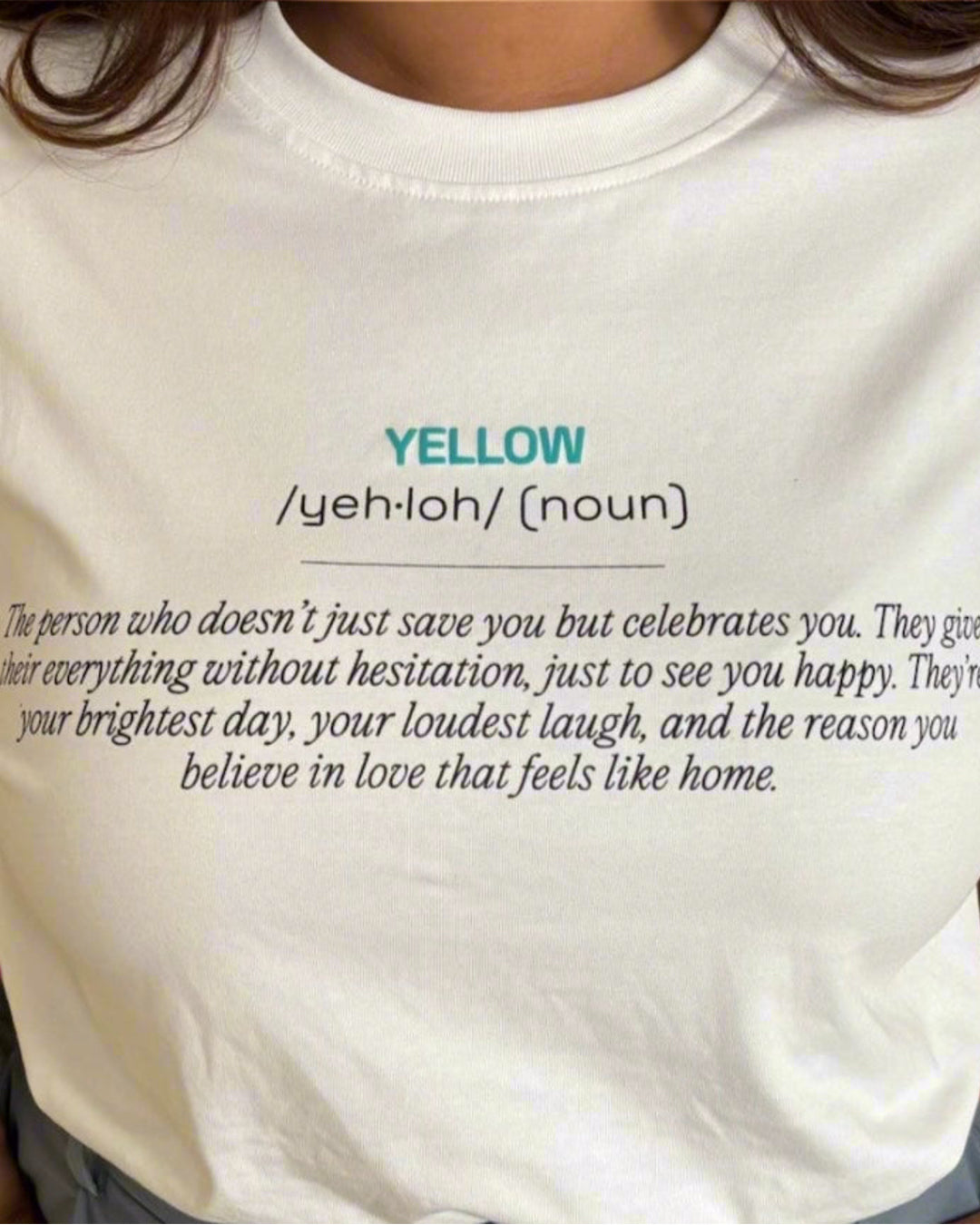 Woman standing wearing a White t-shirt, with yellow and its meaning written in the front